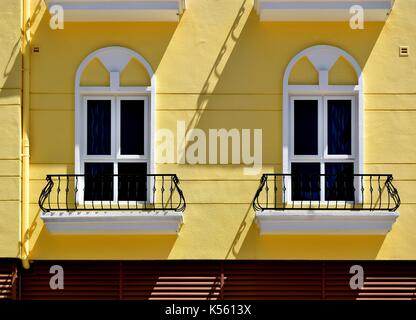In der Nähe von ein paar weiße Fenster mit Metall Balkone auf gelbe Fassade mit dramatischen Schatten Stockfoto