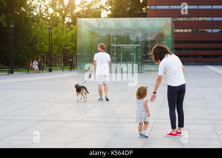 Vereinigte Familie auf einem Spaziergang im Stadtpark. Junge Mann ist ein Hund an der Leine, eine Frau hält die Hand zu einer kleinen Tochter. Stockfoto