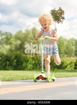 Kleines Mädchen reiten einen Roller im Park Stockfoto