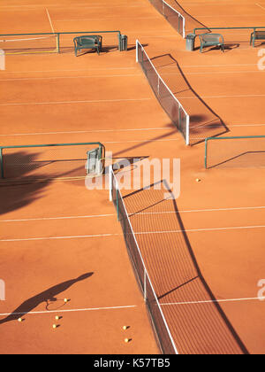 Schatten der Tennisspieler an Net mit scatttered Tennis Bälle auf Sandplatz Stockfoto