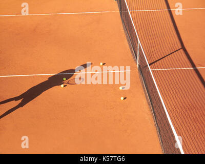 Schatten der Tennisspieler an Net mit scatttered Tennis Bälle auf Sandplatz Stockfoto