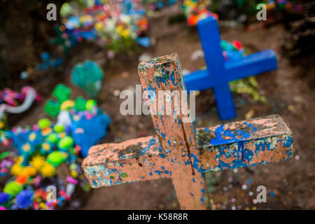 Ein schweres Kreuz, mit Rieselten blaue Farbe, ist unter Bunt geschmückte Gräber während der Tag der Toten Festlichkeiten gesehen auf dem Friedhof in Izalco, Stockfoto