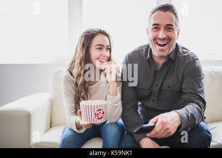 Porträt eines jungen Mannes und Tochter Fernsehen beim Essen Popcorn auf dem Sofa Stockfoto