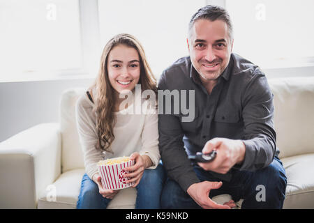 Porträt eines jungen Mannes und Tochter Fernsehen beim Essen Popcorn auf dem Sofa Stockfoto