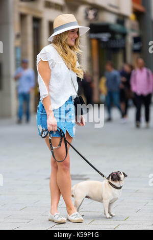 Hübsche junge Frau steht mit einem Mops auf einem Bürgersteig in der Stadt Stockfoto