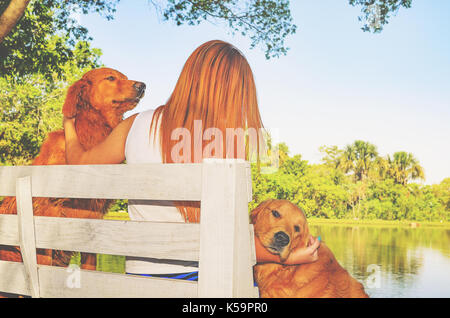 Mädchen mit roten Haaren auf einer Bank, die von einem Bauernhof mit ihren beiden Hunden sitzen. Mädchen Zeit, dabei darauf achten, die Aufmerksamkeit auf Ihre vierbeinigen Begleiter auf eine na Stockfoto