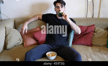 Junger Mann auf der Couch Bier trinken und Essen Stockfoto