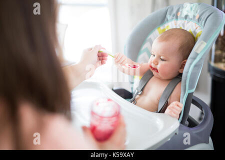 Mutter Feeding Baby Mädchen in hoher Stuhl Stockfoto