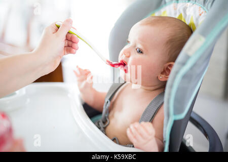 Mutter Feeding Baby Mädchen in hoher Stuhl Stockfoto