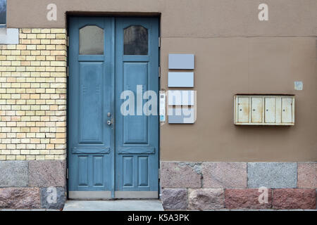 Die Wand eines alten Bürogebäude aus gelben Backsteinen, rotem Granit und braun Gips. Blaue Tür und leere Mieter banner Vorderansicht Stockfoto
