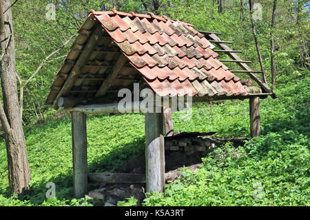 Eine ohne Wände Halle für die Lagerung von Brennholz liegt am Hang eines Hügels liegt. Feder sonnigen Tag Stockfoto