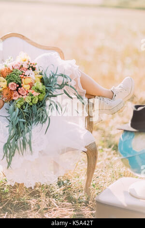 Die vertikale Nahaufnahme der Beine der Braut und der riesigen wedding bouquet auf dem Hintergrund des Feldes. Stockfoto