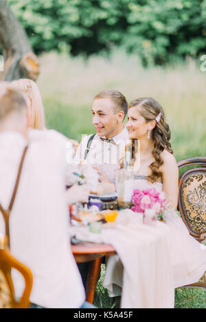 Die Seite vertikale Foto der Brautjungfer in der langen rosa Kleid und der beste Mann mit dem Schmetterling auf der Hochzeit Tisch sitzen. Stockfoto