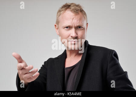 Ein junger Mann mit zerzausten Haar und schwarze Kleidung, schaut die Kamera in Unmut. Stockfoto