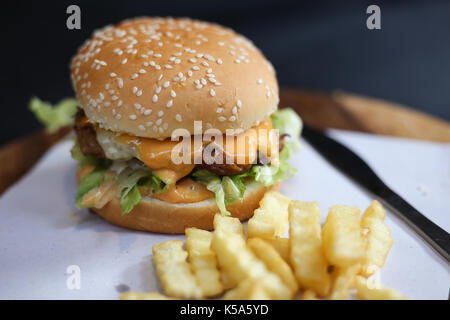 Hamburger mit Pommes frites auf einem Holzteller serviert. Stockfoto