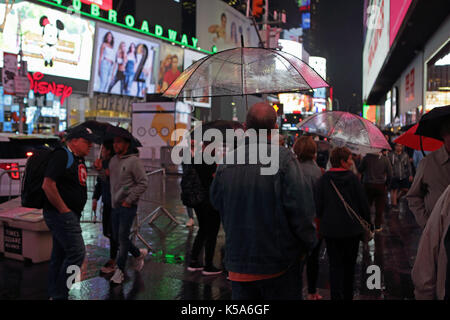 Regnerischen Nacht in Times Square, Touristen mit Sonnenschirmen gehen 7. Avenue und Broadway hell erleuchtet durch elektrische Plakatwerbung Bildschirme Stockfoto