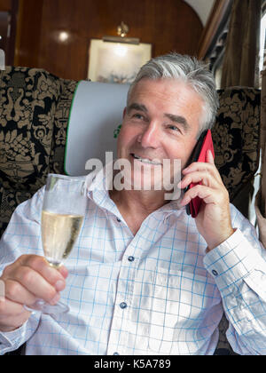 Luxus Champagner zug Mann mit einem Glas Champagner, über sein Smartphone, genießen eine Fahrt in der ersten Klasse vintage Pullman Waggon Stockfoto