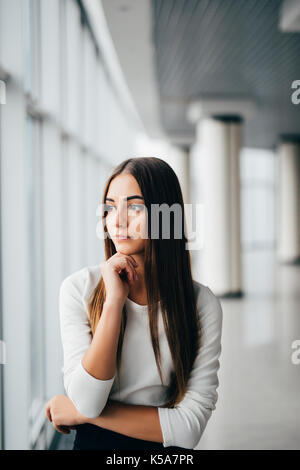 Attraktive junge geschäftsfrau mit den Händen auf das Kinn in der Nähe von Office windows Stockfoto