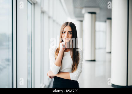 Attraktive junge geschäftsfrau mit den Händen auf das Kinn in der Nähe von Office windows Stockfoto