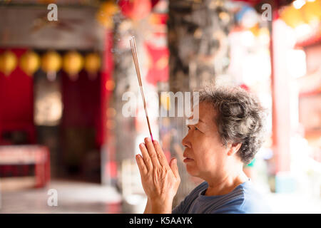 Ältere Frau zu beten Buddha mit Räucherstäbchen an Tempel Stockfoto