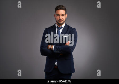 Ein zuversichtlich elegante hübscher junger Mann steht vor einem grauen Hintergrund in einem Studio einen schönen Anzug tragen Stockfoto
