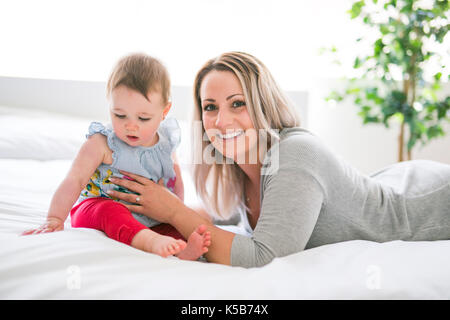 Hübsches Baby Sit-on-Mom im seidenen Bett Stockfoto