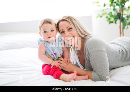 Hübsches Baby Sit-on-Mom im seidenen Bett Stockfoto