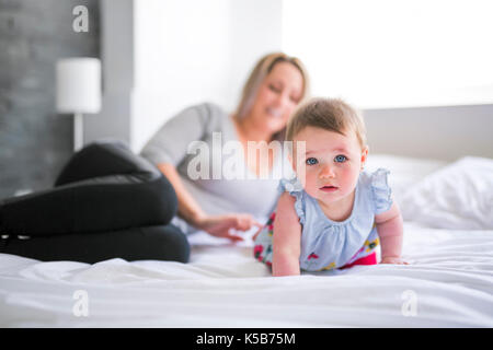 Hübsches Baby Sit-on-Mom im seidenen Bett Stockfoto