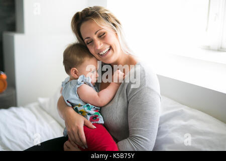 Hübsches Baby Sit-on-Mom im seidenen Bett Stockfoto