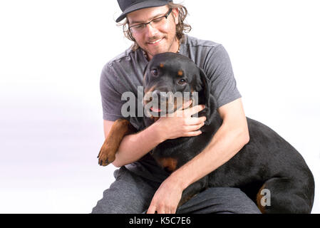 Glücklicher Hund Eigentümer Holding ein Rottweiler mit Sweet Expression auf weißem Hintergrund Stockfoto