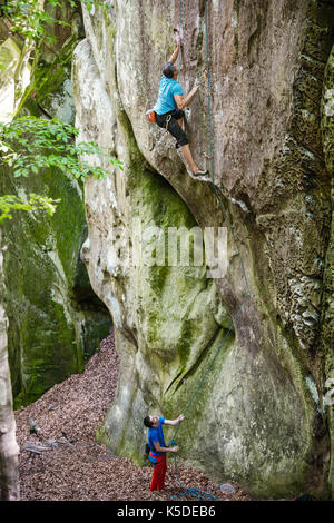 Junger Mann an der senkrechten Felsen, seinem Partner sichern. Top Rope klettern. Stockfoto