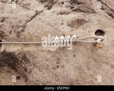 Bügeleisen verdrilltes Seil zwischen die Felsen in Kletterer gestreckt patch Klettersteig. Seil fest im Block durch Schrauben Karabinerhaken. Detail der Tampen in s verankert Stockfoto