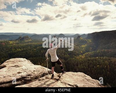 Happy Tourist mit unterarm Krücke über den Kopf erreicht Berggipfel. Wanderer mit verletzten Knie in "Wegfahrsperre und Medizin Polen halten Sie die Hand in die Luft. Colorfu Stockfoto