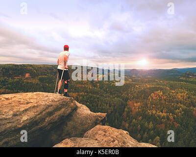 Man touristische nach Unfall mit knieorthese Funktionen und Unterarm Krücken. Mann mit Blick über das Tal der Sonne am Horizont hängen. Stockfoto