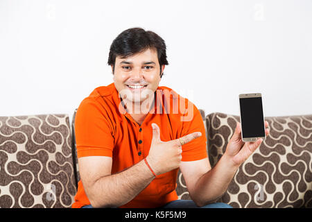 Indische Mann sitzt auf einem Sofa und am Handy zu Hause zeigen Stockfoto