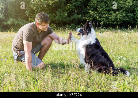 Hohe fünf mit der Süße Border Collie und ein junger Mann im Freien. Stockfoto