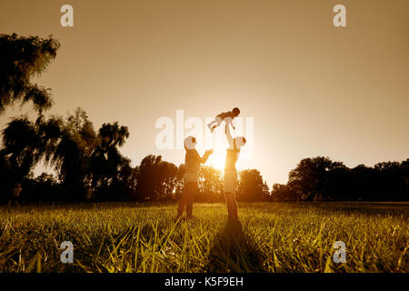 Happy Family spielen mit einem Kind bei Sonnenuntergang im Park. Stockfoto