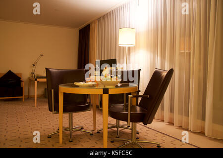 Wien, ÖSTERREICH - Apr 28th, 2017: Romantischer Abend mit einer Flasche Rotwein, Süßigkeiten und Früchte im Luxus Hotel Zimmer auf eine Tabelle mit 3 Lederstühlen, Hilton Penthouse Suite Stockfoto