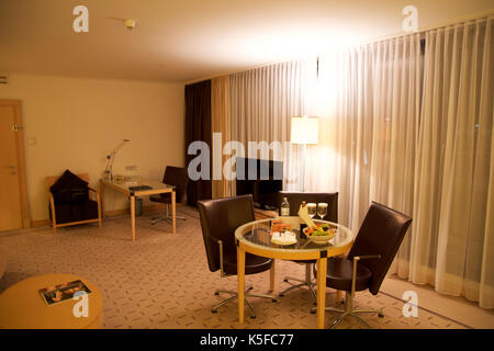 Wien, ÖSTERREICH - Apr 28th, 2017: Romantischer Abend mit einer Flasche Rotwein, Süßigkeiten und Früchte im Luxus Hotel Zimmer auf eine Tabelle mit 3 Lederstühlen, Hilton Penthouse Suite Stockfoto