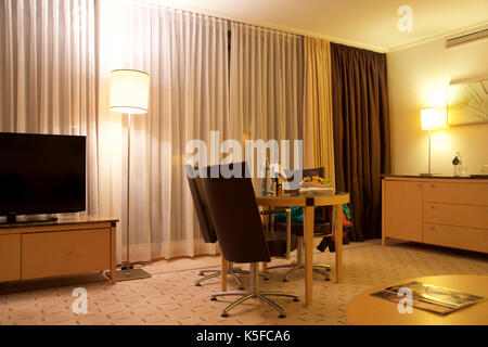 Wien, ÖSTERREICH - Apr 28th, 2017: Romantischer Abend mit einer Flasche Rotwein, Süßigkeiten und Früchte im Luxus Hotel Zimmer auf eine Tabelle mit 3 Lederstühlen, Hilton Penthouse Suite Stockfoto