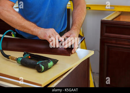 Tischler Brad mit Nagelpistole, Crown Moulding auf Küchenschränke framing trim mit dem Warnhinweis, dass alle Elektrowerkzeuge Illus auf sie gezeigt haben Stockfoto