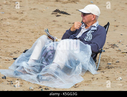 Swanage, Dorset, Großbritannien. 9 Sep, 2017. UK Wetter: Starker Regen und Donner, durchsetzt mit Sonnenschein in Swanage. Älterer Mann im Sessel sitzend mit Beinen in Plastikfolien auf den Strand fallen. Credit: Carolyn Jenkins/Alamy leben Nachrichten Stockfoto