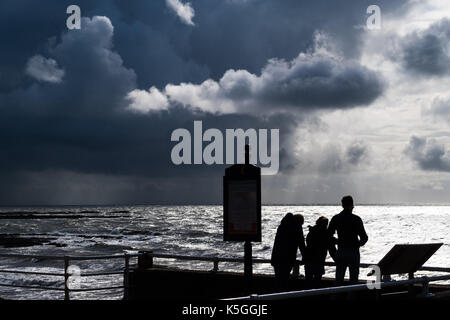 Aberystwyth Wales UK, Samstag, 09. September 2017 UK Wetter: eine Gruppe von drei Personen in Silhouette den Wellen zusehen, wie dunkel brütende Gewitterwolken, schwere mit der Drohung der sintflutartigen Regenfälle, versammeln sich in den Himmel über dem turbulenten Meer in Aberystwyth an der Küste der Cardigan Bay in West Wales Foto © Keith Morris/Alamy leben Nachrichten Stockfoto