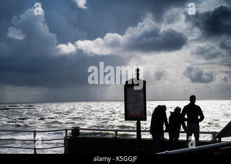 Aberystwyth Wales UK, Samstag, 09. September 2017 UK Wetter: eine Gruppe von drei Personen in Silhouette den Wellen zusehen, wie dunkel brütende Gewitterwolken, schwere mit der Drohung der sintflutartigen Regenfälle, versammeln sich in den Himmel über dem turbulenten Meer in Aberystwyth an der Küste der Cardigan Bay in West Wales Foto © Keith Morris/Alamy leben Nachrichten Stockfoto