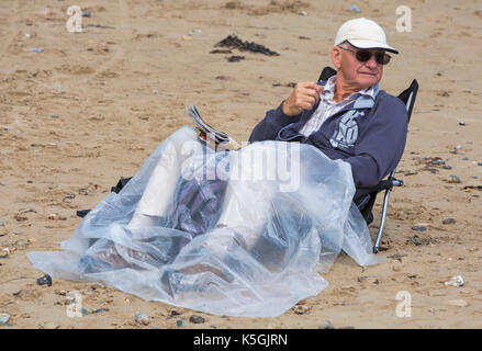 Swanage, Dorset, Großbritannien. 9 Sep, 2017. UK Wetter: Starker Regen und Donner, durchsetzt mit Sonnenschein in Swanage. Älterer Mann im Sessel sitzend mit Beinen in Plastikfolien auf den Strand fallen. Credit: Carolyn Jenkins/Alamy leben Nachrichten Stockfoto