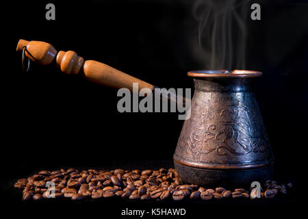 Alte türkische Kaffeemaschine auf einem schwarzen Hintergrund mit Kaffeebohnen. Stockfoto