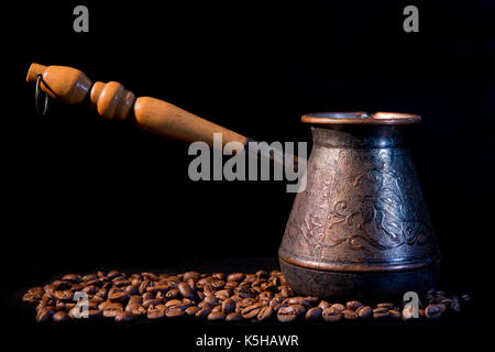 Alte türkische Kaffeemaschine auf einem schwarzen Hintergrund mit Kaffeebohnen. Stockfoto