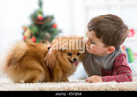 Kleines Kind Junge mit Hund liegend auf dem Boden Weihnachtsbaum Stockfoto