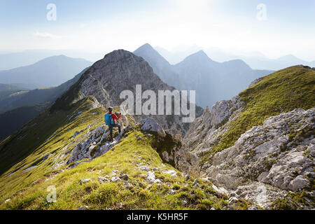 Frau in der roten Jacke, mit Wanderstöcken und Rucksack Wanderungen bis zu einem Aussichtspunkt auf Kladivo, Karawanken, Slowenien. Stockfoto