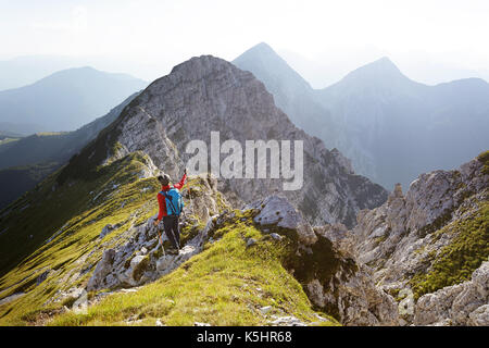 Frau mit einer Mütze und roten windstopper an Berge, die auf einer steilen felsigen Gipfel. Kladivo, Karawanken, Slowenien. Stockfoto